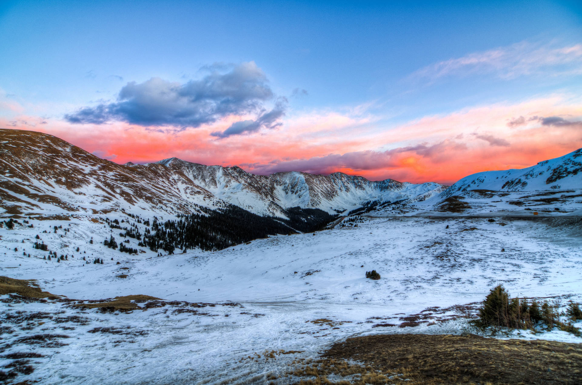 Fjellsolnedgang med land dekket av snø og en oransje himmel.