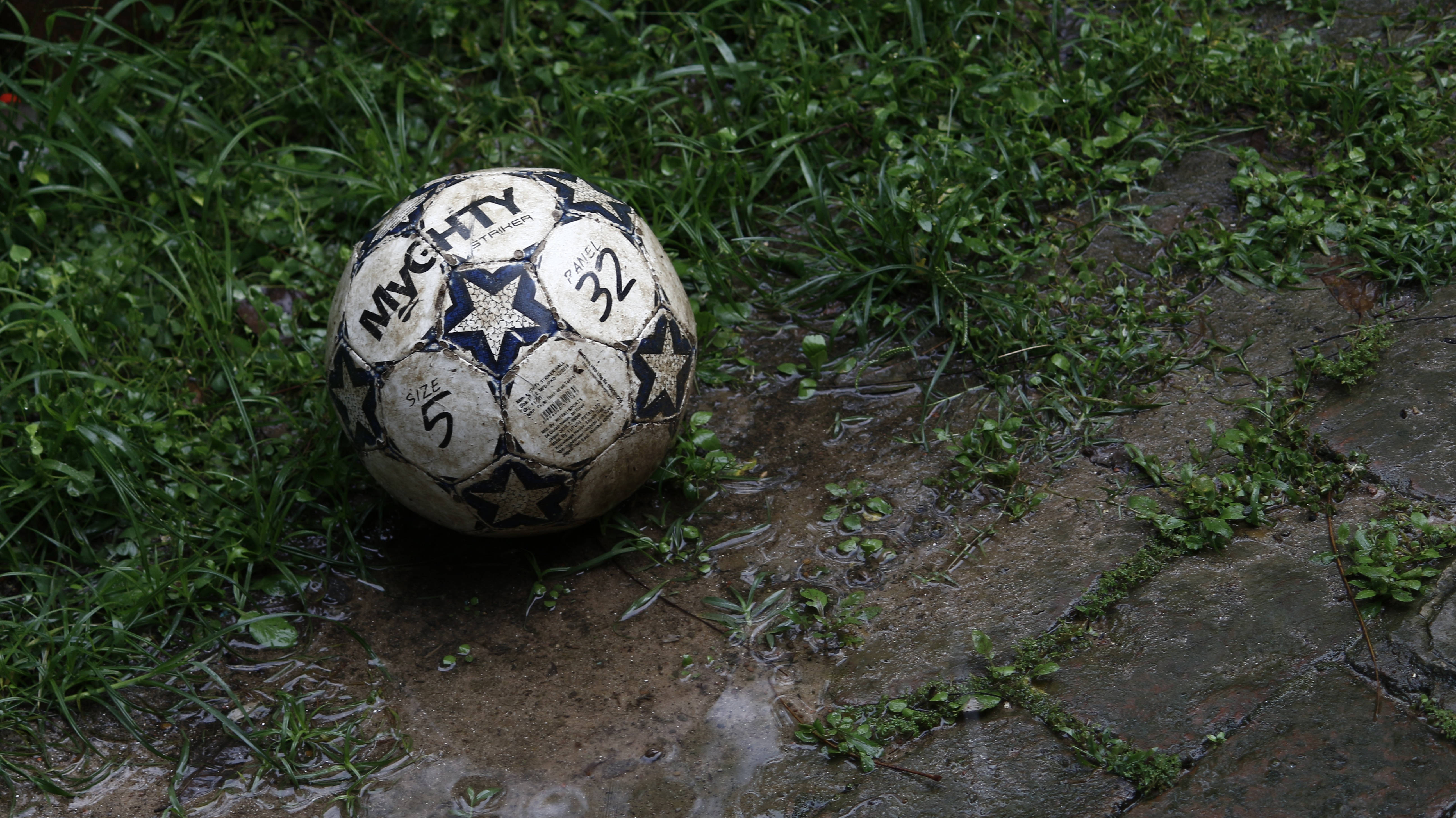 En gjørmete fotball ligger uavhentet i gresset. Bakgrunner