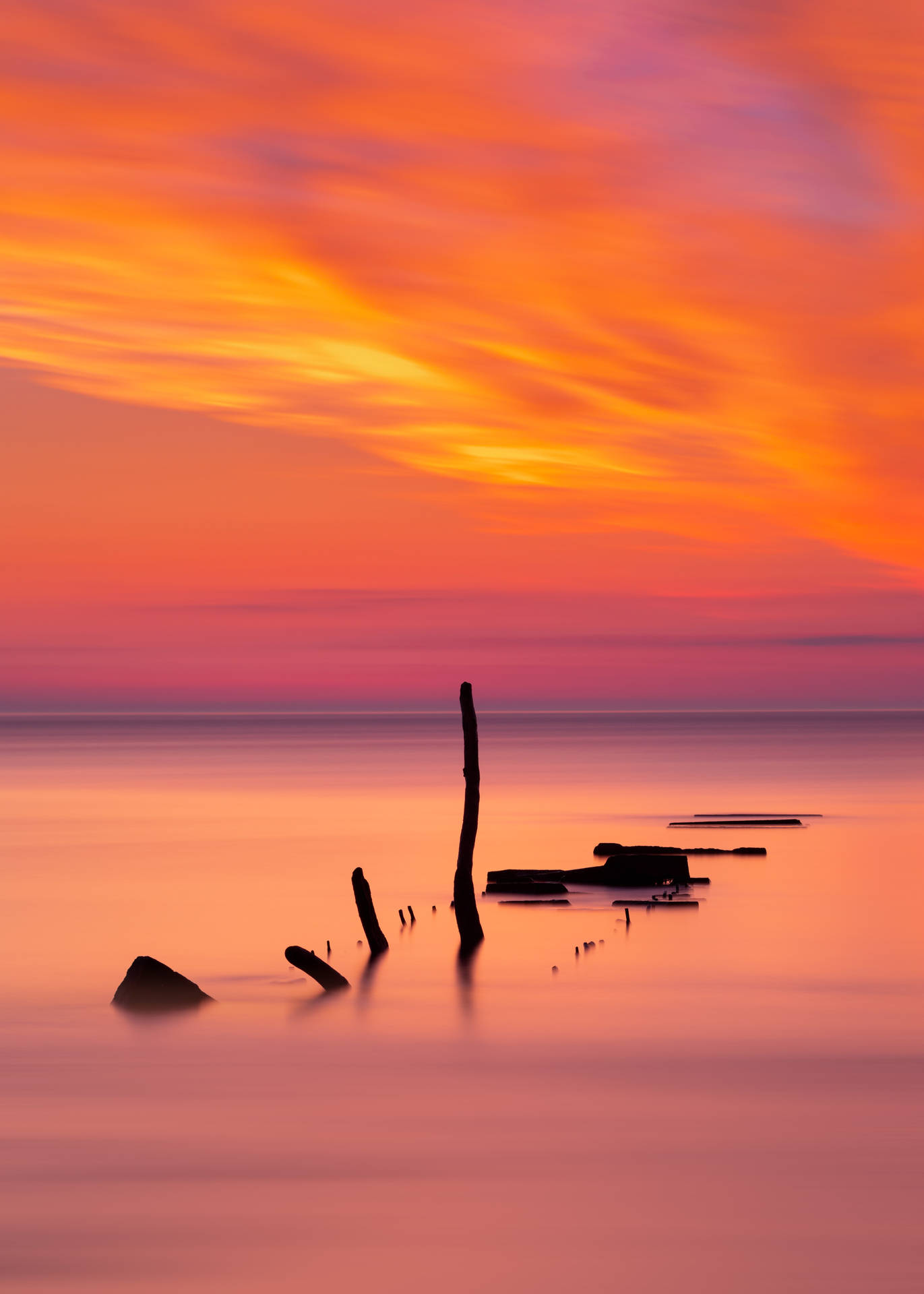 Hav med oransje og rosa horisont under solnedgang og pinner som flyter.