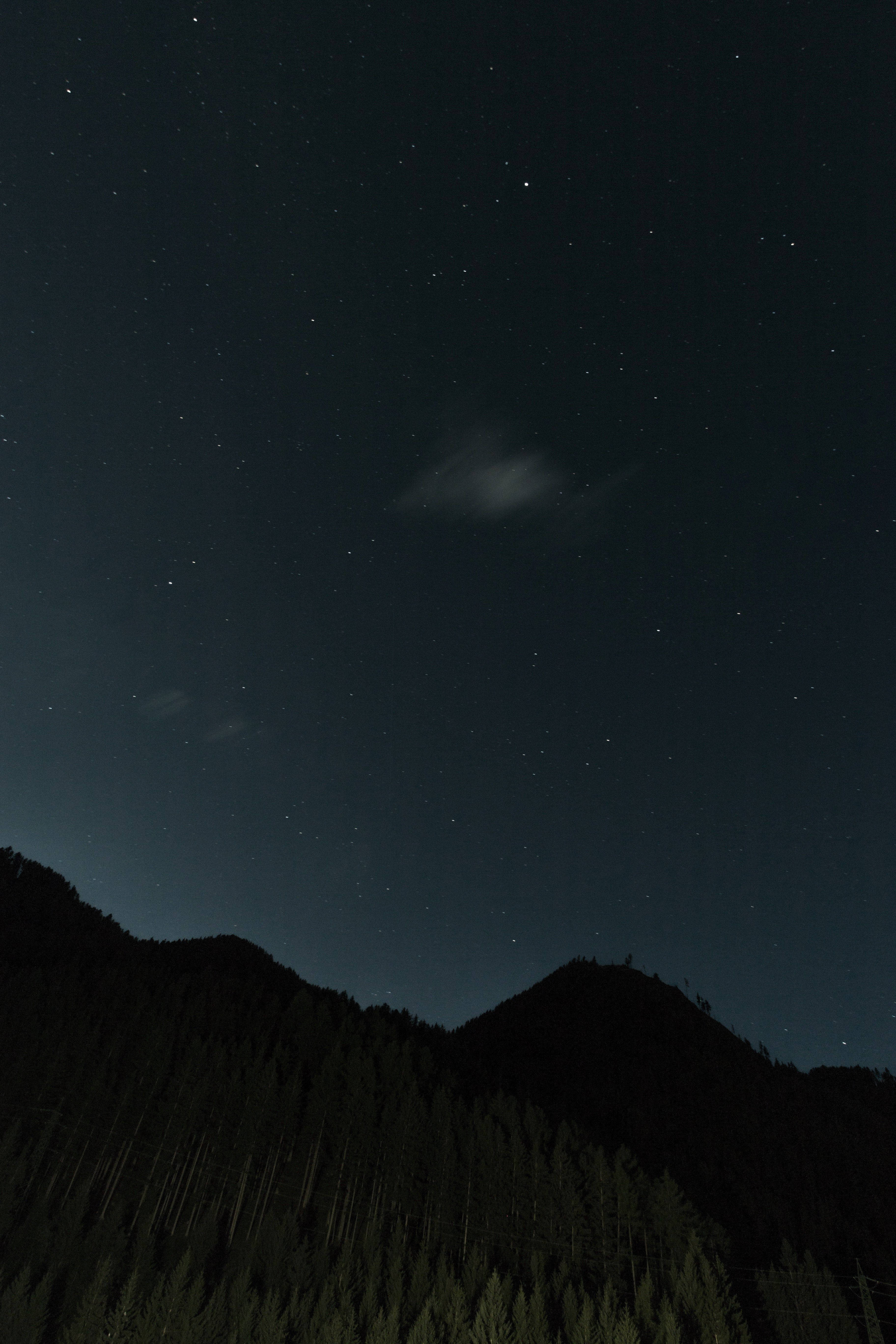 En svakt opplyst, stjernefylt himmel over en fantastisk fjellsilhuett. Bakgrunner