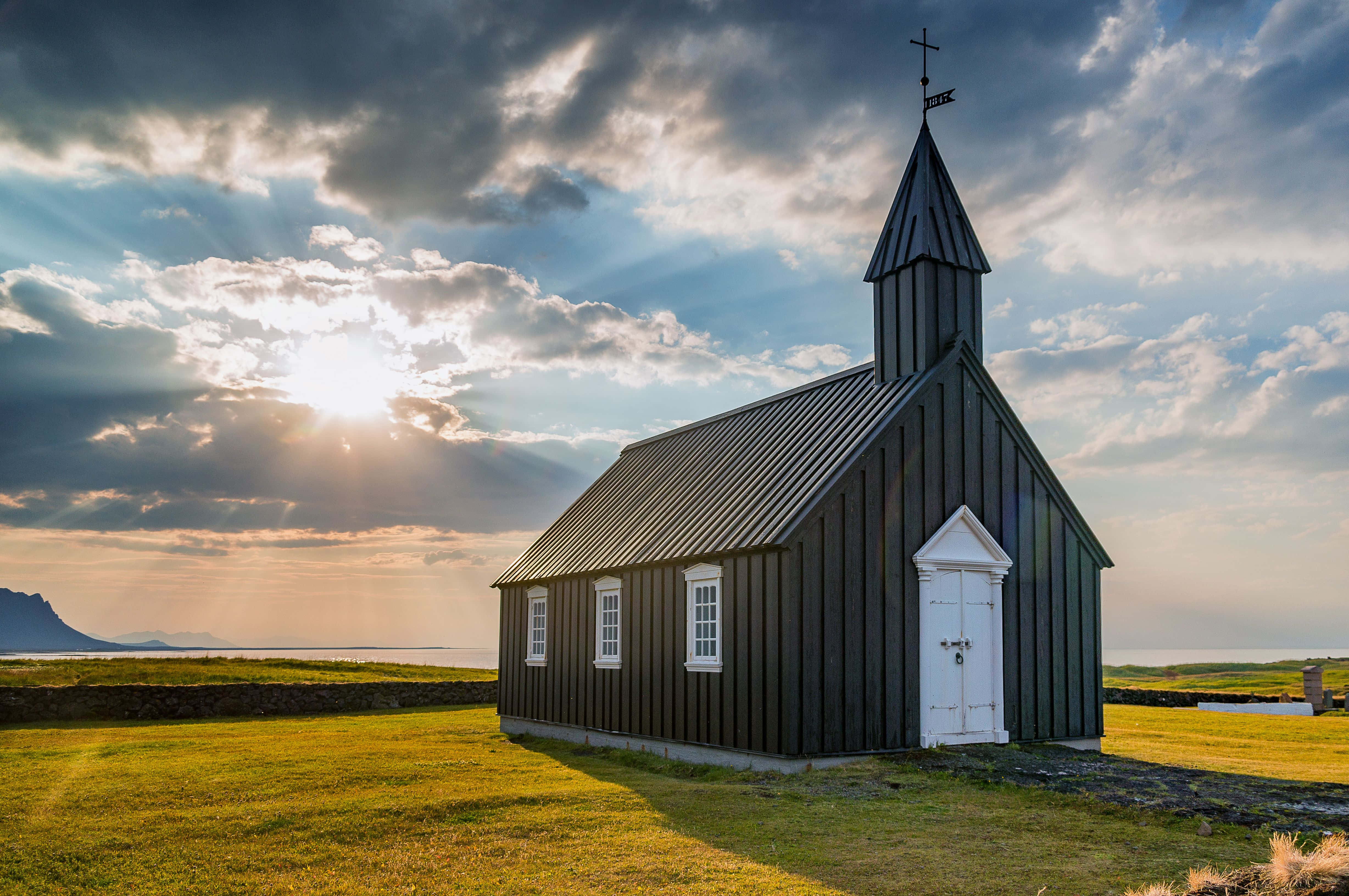 en svart kirke ligger på en gresslette Bakgrunner