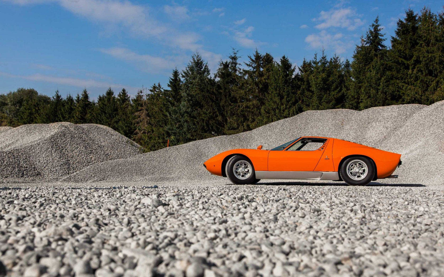 En utsøkt oransje Lamborghini Miura på en grusvei. Bakgrunner
