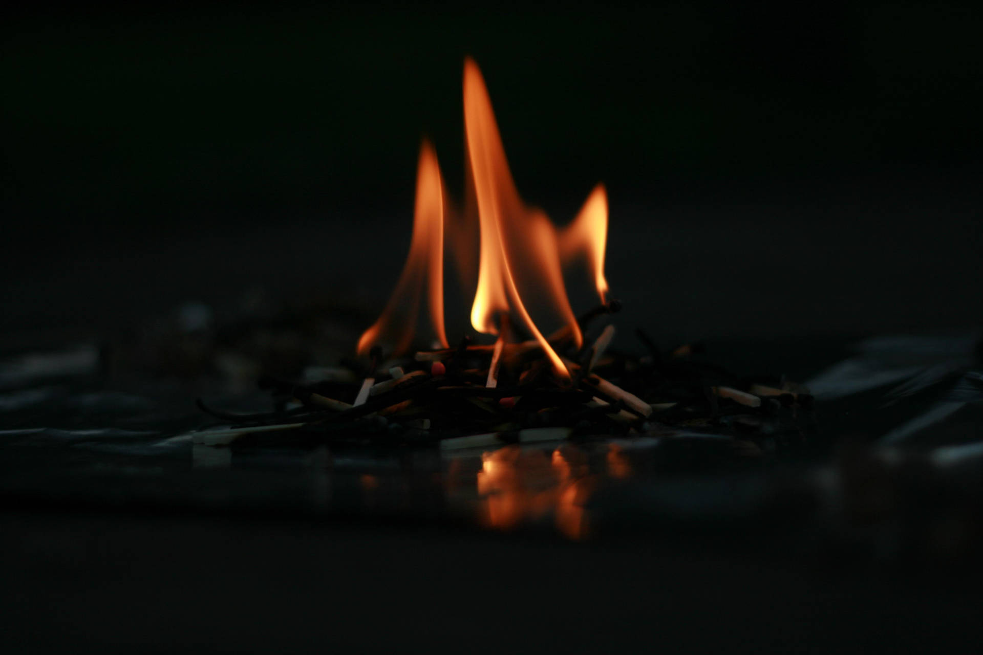 Små fyrstikker tent med dempet skarpe rødoransje flammer på gulvet inne i et mørkt rom.