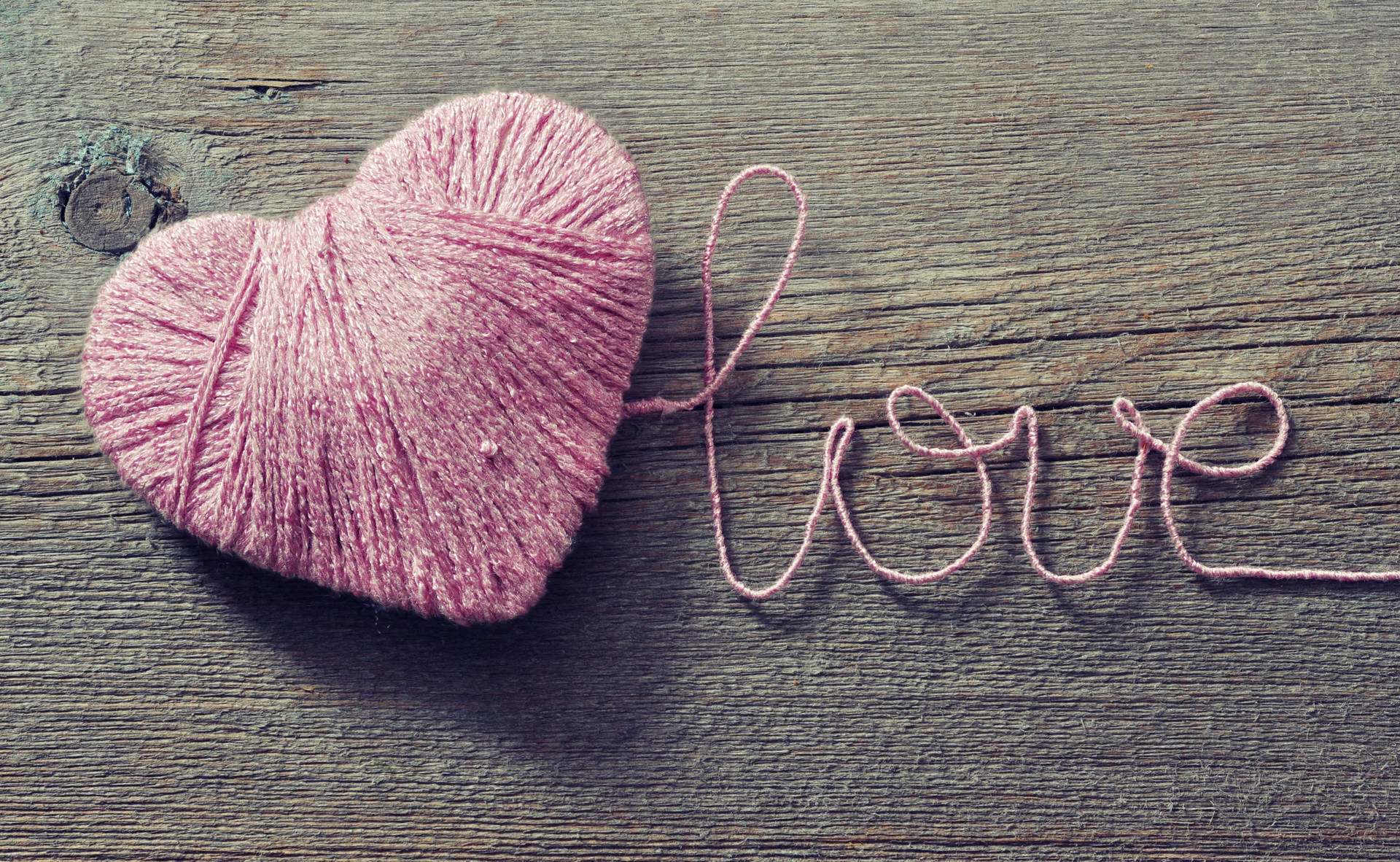 Romantisk ord «Love» skrevet med rosa snor som danner et hjerte på trebord for Valentinsdagen.