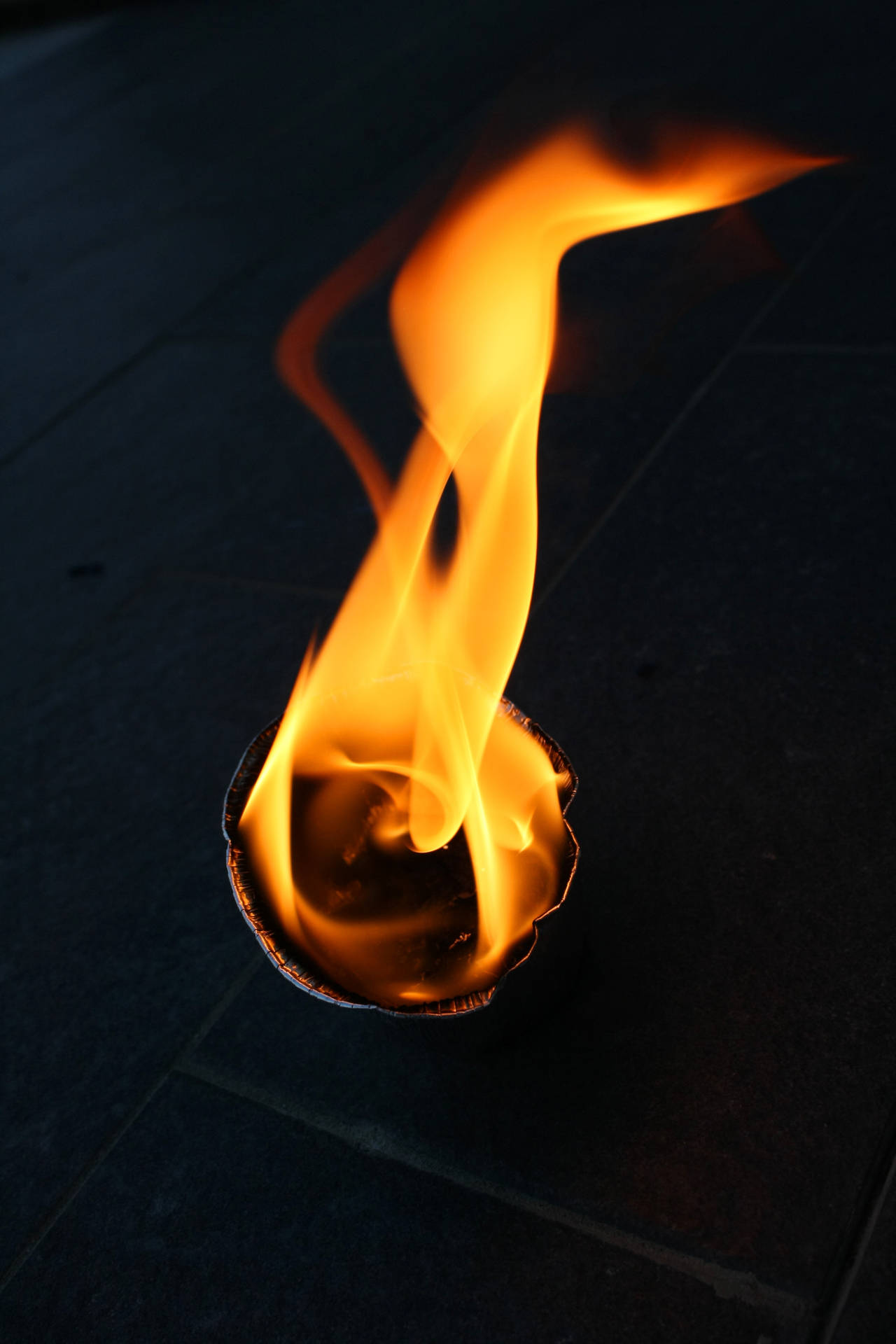 Rundt papirstykke som brenner på gulvet. Nærbilde av ildflamme. Noe som brenner inne i et mørkt rom.