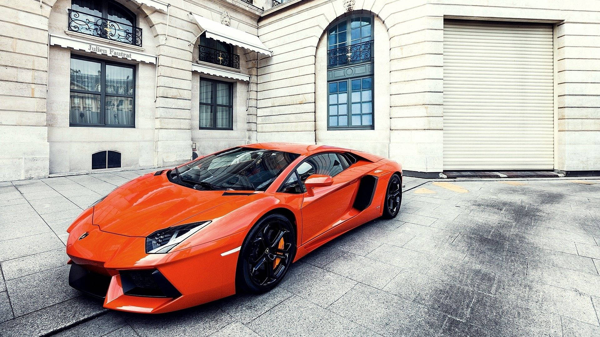 Oransje Lamborghini Aventador med bygningsbakgrunn.