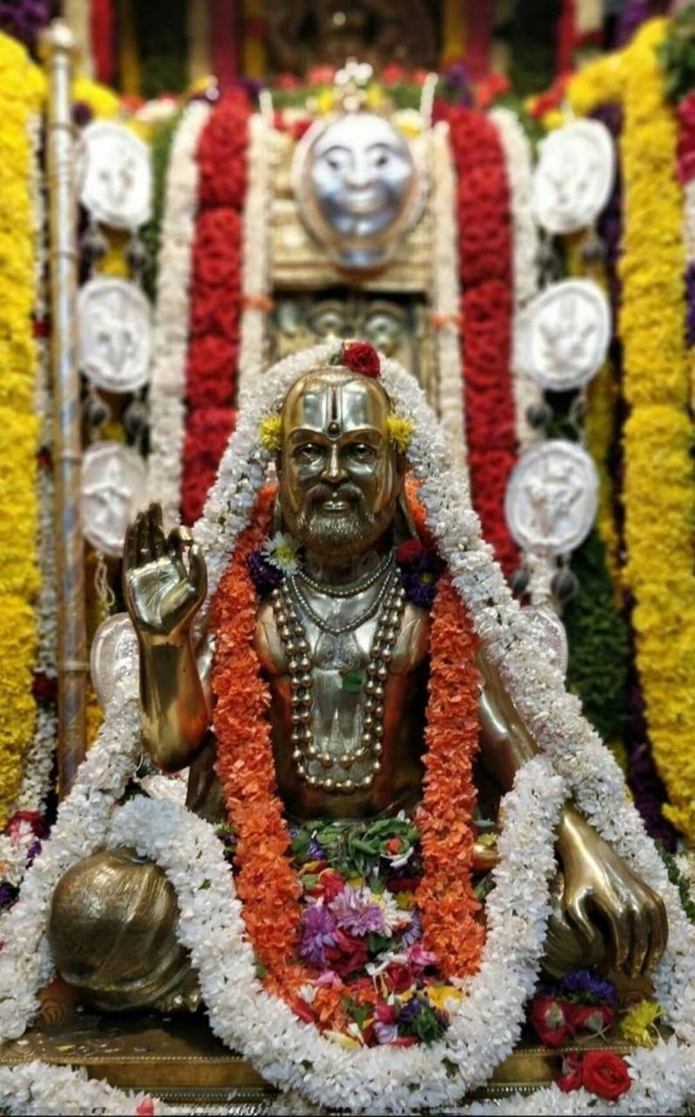 Majestetisk gullstatue av Raghavendra prydet med blomsterkranser Bakgrunner
