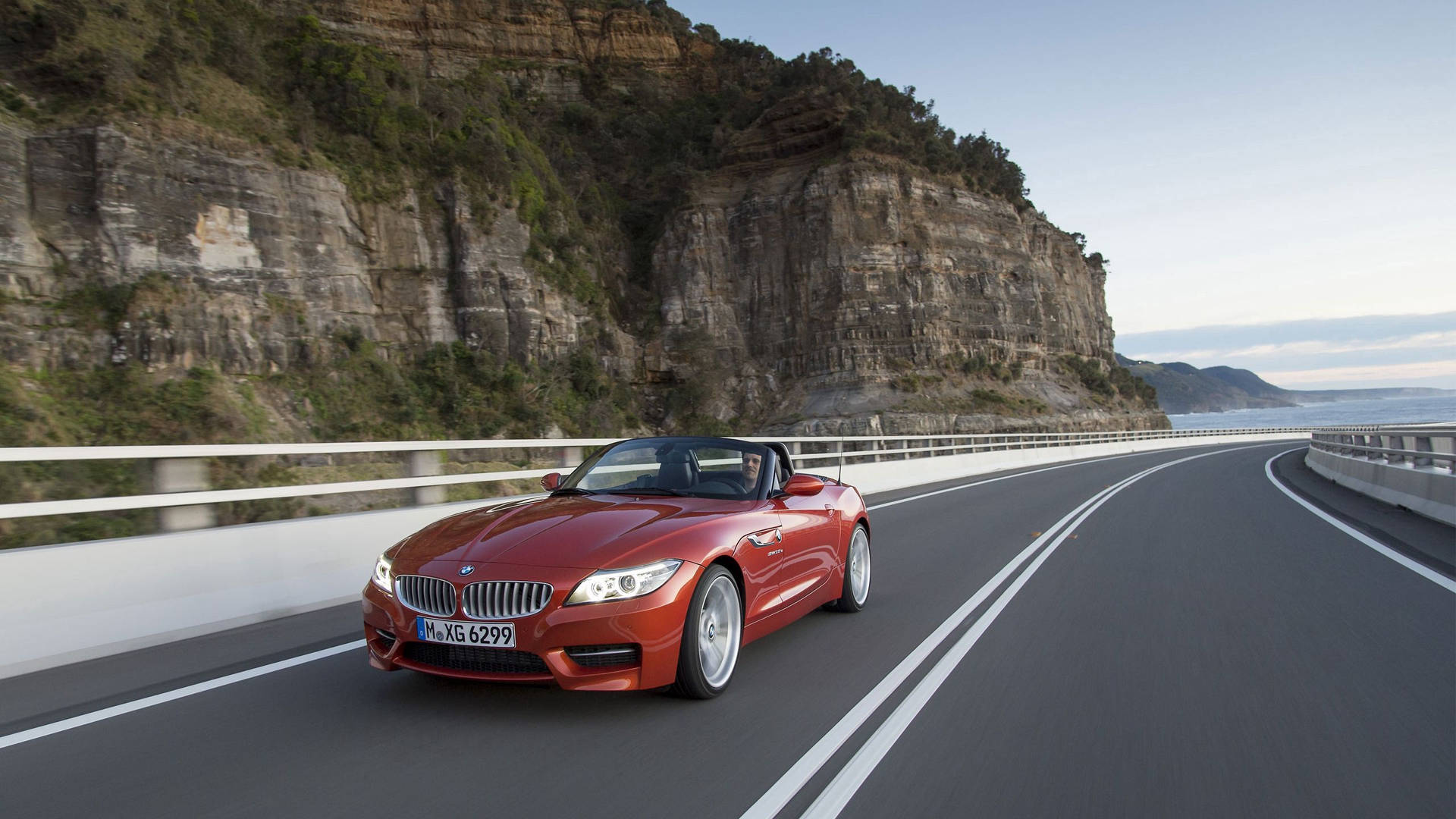 Oransje BMW Z4 på vei ved siden av fjell bakgrunnsbilde