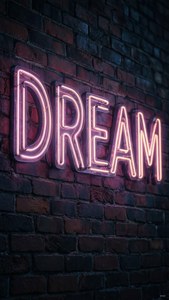 Et neonskilt med 'DREAM' på en murvegg om natten, stemningsfullt og kunstnerisk. — iPad Bakgrunner