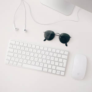 Minimalistisk bakgrunnsbilde av hvitt Apple MAC-oppsett bestående av iMAC, trådløst tastatur, magisk mus og hodetelefon.