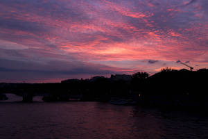 Solnedgang ved havkanten med mørke trær og hus.