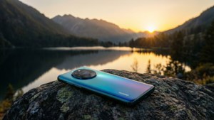 Huawei-telefon på en stein med utsikt over en fjellinnsjø ved solnedgang, rolig landskap.