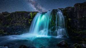 Lysende foss under en stjerneklar nattehimmel med dype svarttoner.