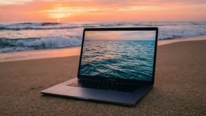 En rolig MacBook på en strand under soloppgang med havtoner.